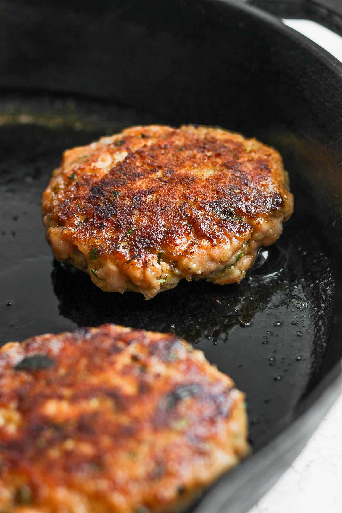 Salmon burgers cooking in a cast iron skillet.