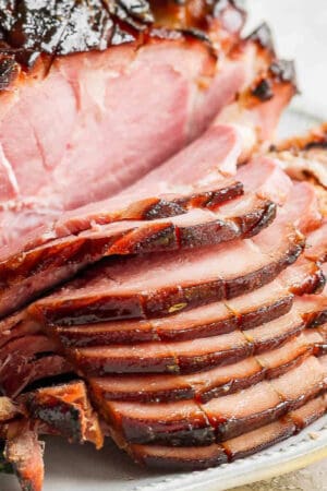 A ham on a plate with part of it sliced.