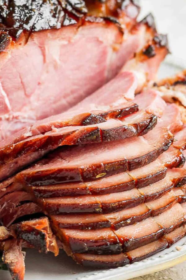 A ham on a plate with part of it sliced.