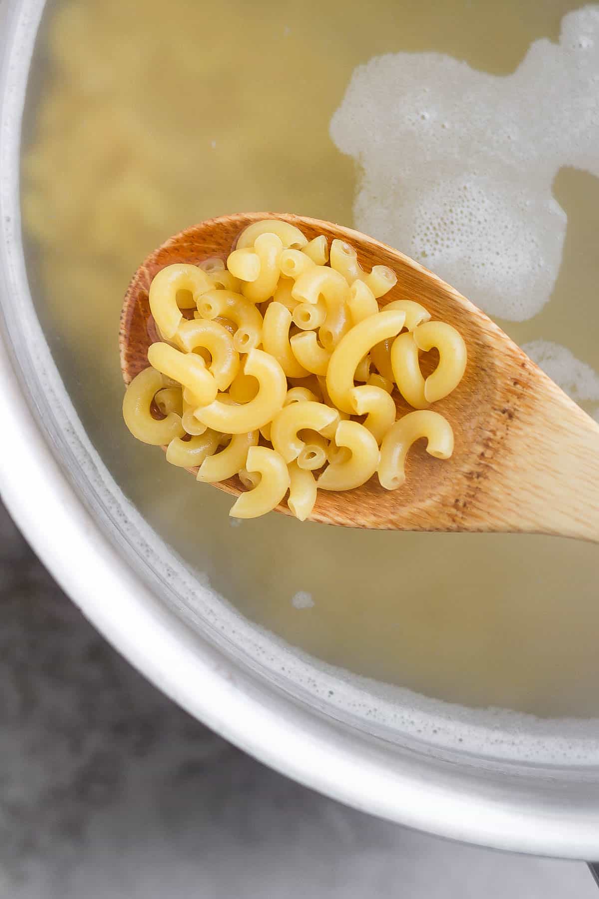 Macaroni noodles being boiled in a pot and a spoon scooping some out.