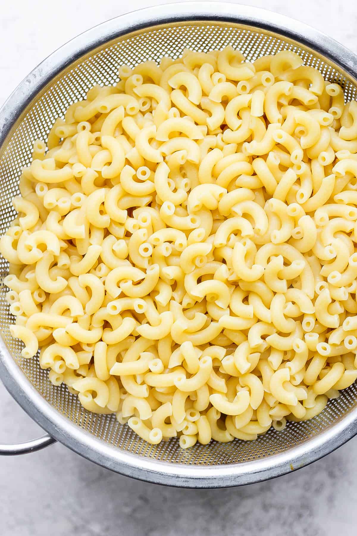 Cooked macaroni noodles draining in a colander.