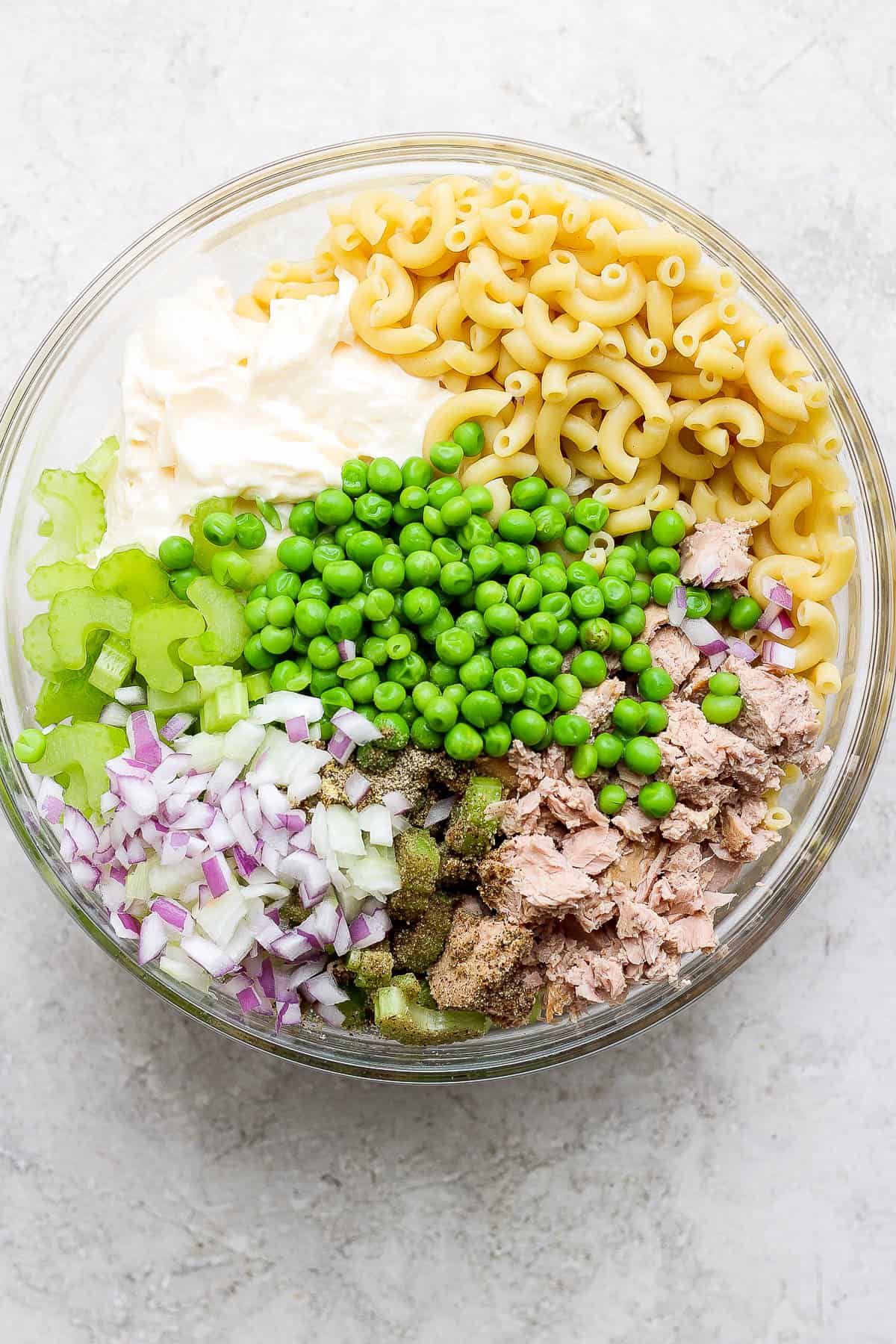All of the tuna macaroni salad ingredients in a large glass bowl.