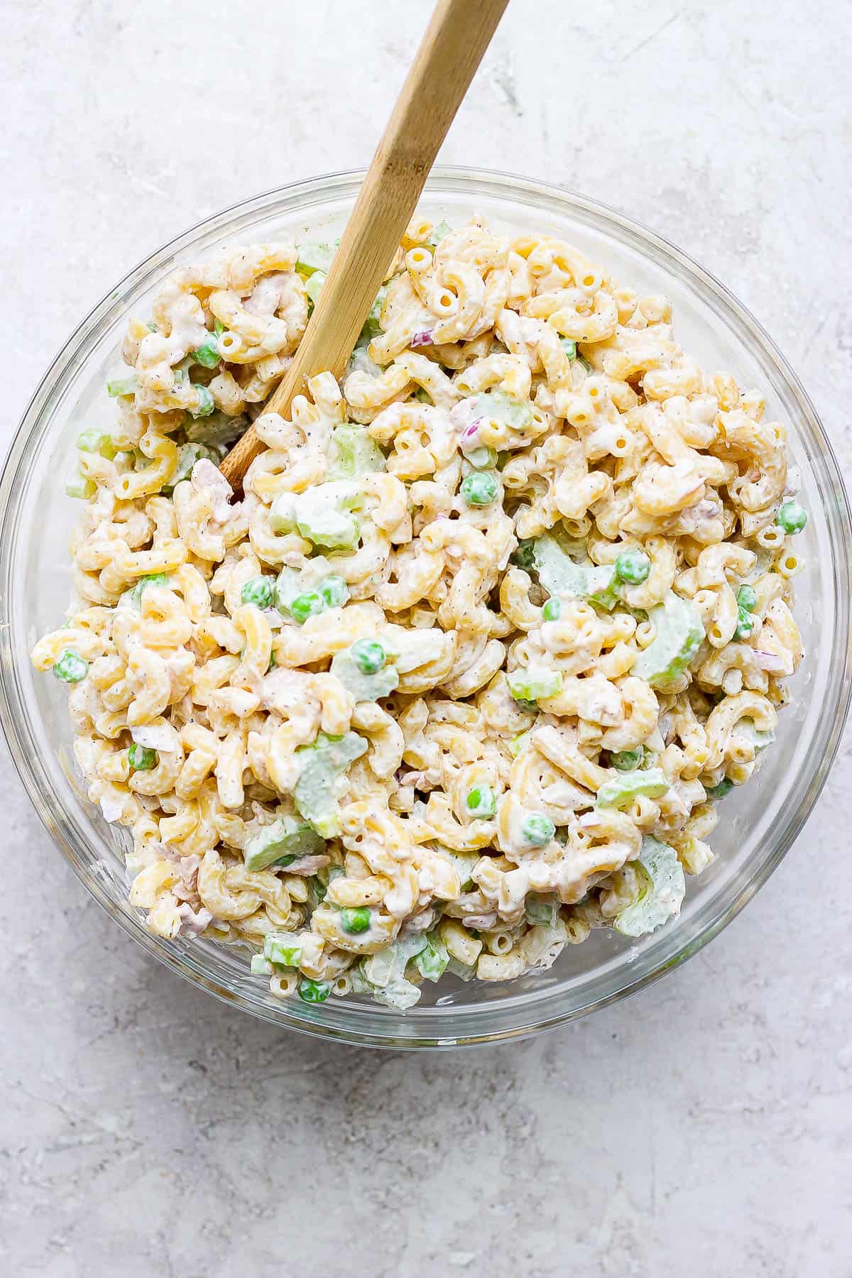 Tuna macaroni salad mixed together in a bowl with a wooden spoon.