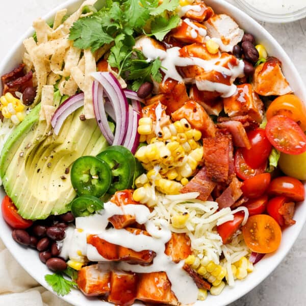 Top down shot of a bowl of bbq chicken salad with avocado, black beans, red onion, corn and tomatoes.