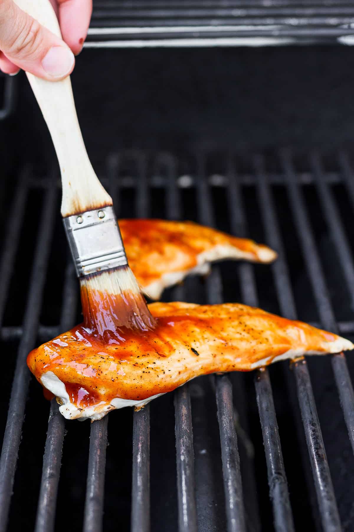 Chicken breasts on the grill being brushed with bbq sauce.