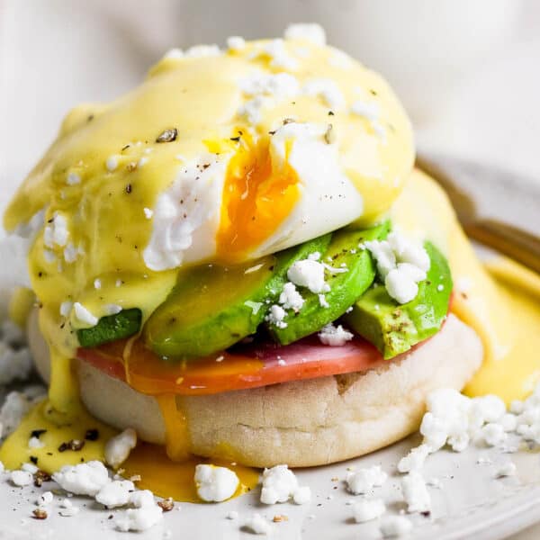 Straight on shot of an eggs benedict recipe with avocado and goat cheese crumbles and runny poached egg on a plate.