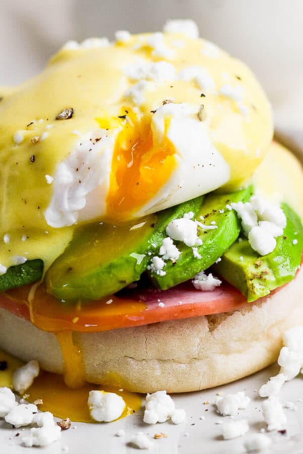 Straight on shot of an eggs benedict recipe with avocado and goat cheese crumbles and runny poached egg on a plate.