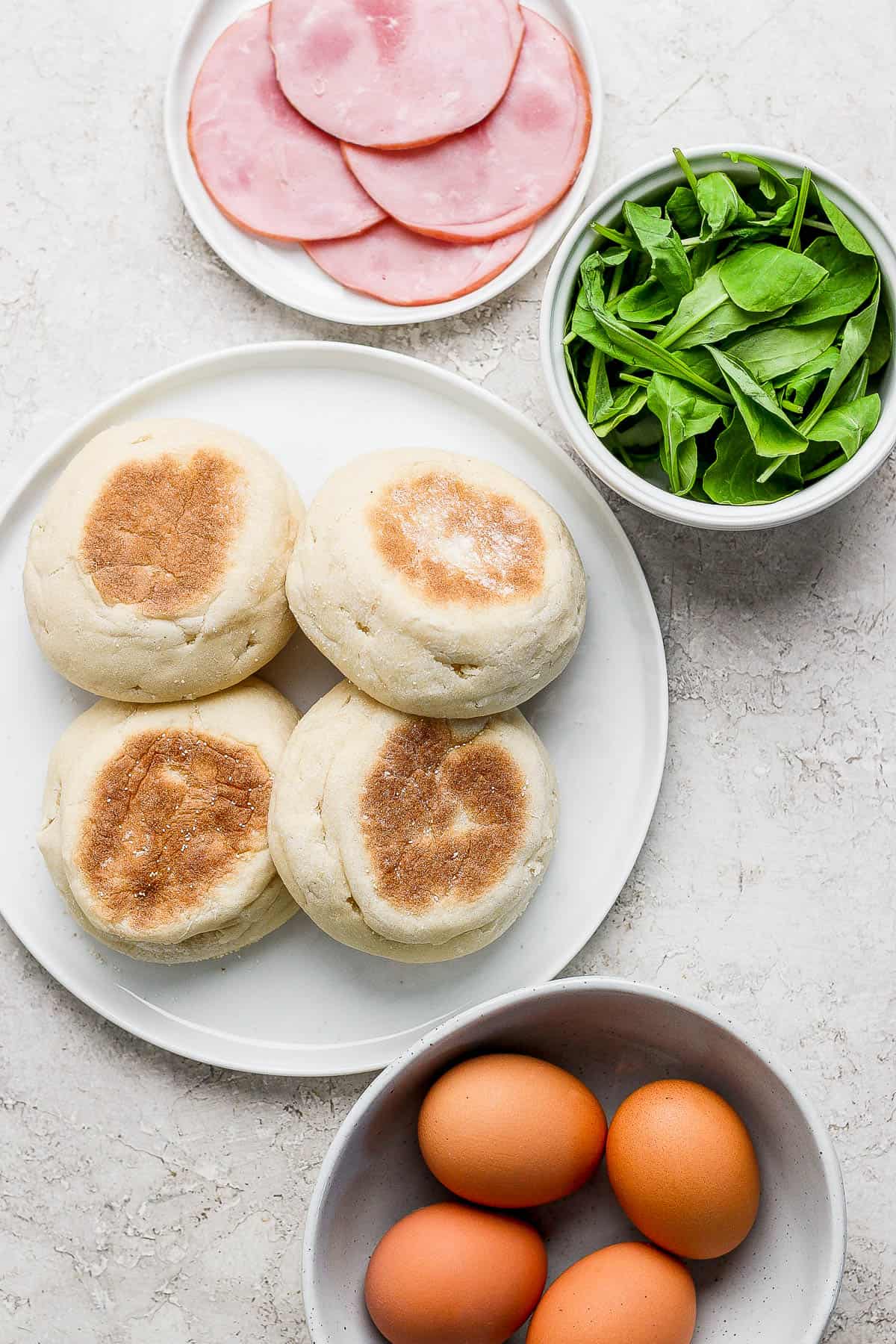 Eggs benedict ingredients on separate plates.