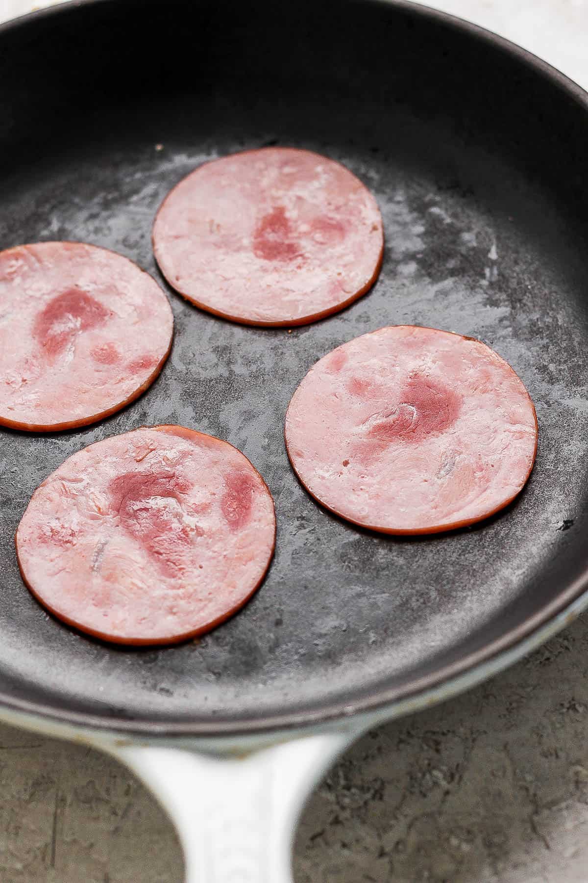 Slices of Canadian bacon in a skillet.