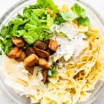 Top down shot of a bowl of caesar pasta salad with bow-tie pasta, parmesan cheese, croutons, dressing and romaine lettuce.