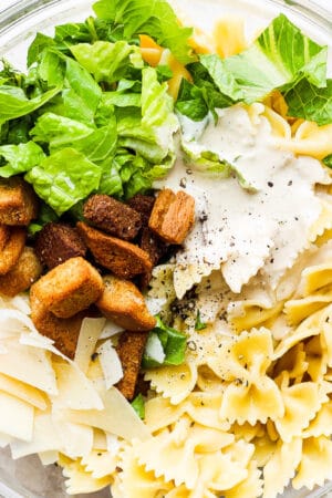 Top down shot of a bowl of caesar pasta salad with bow-tie pasta, parmesan cheese, croutons, dressing and romaine lettuce.