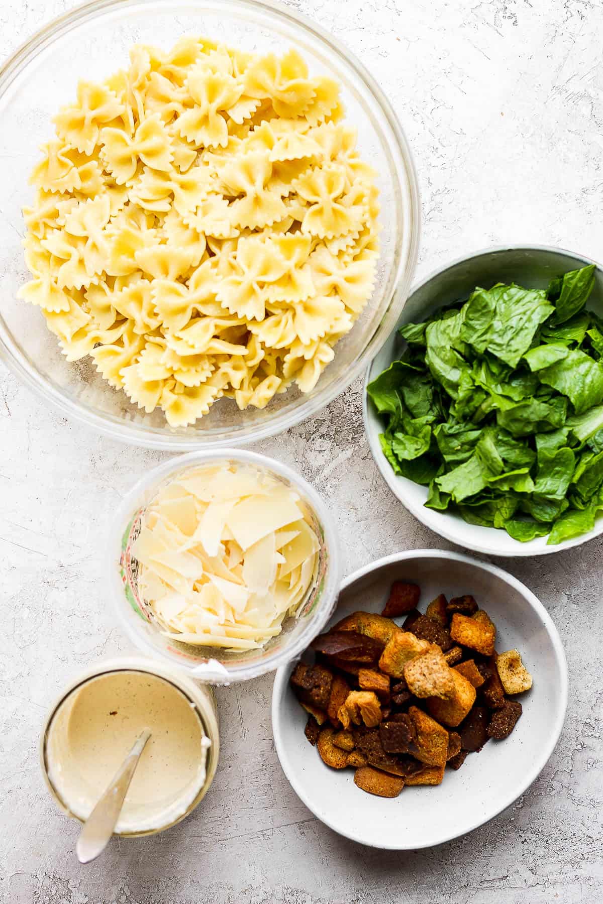 Ingredients for caesar pasta salad in separate bowls.
