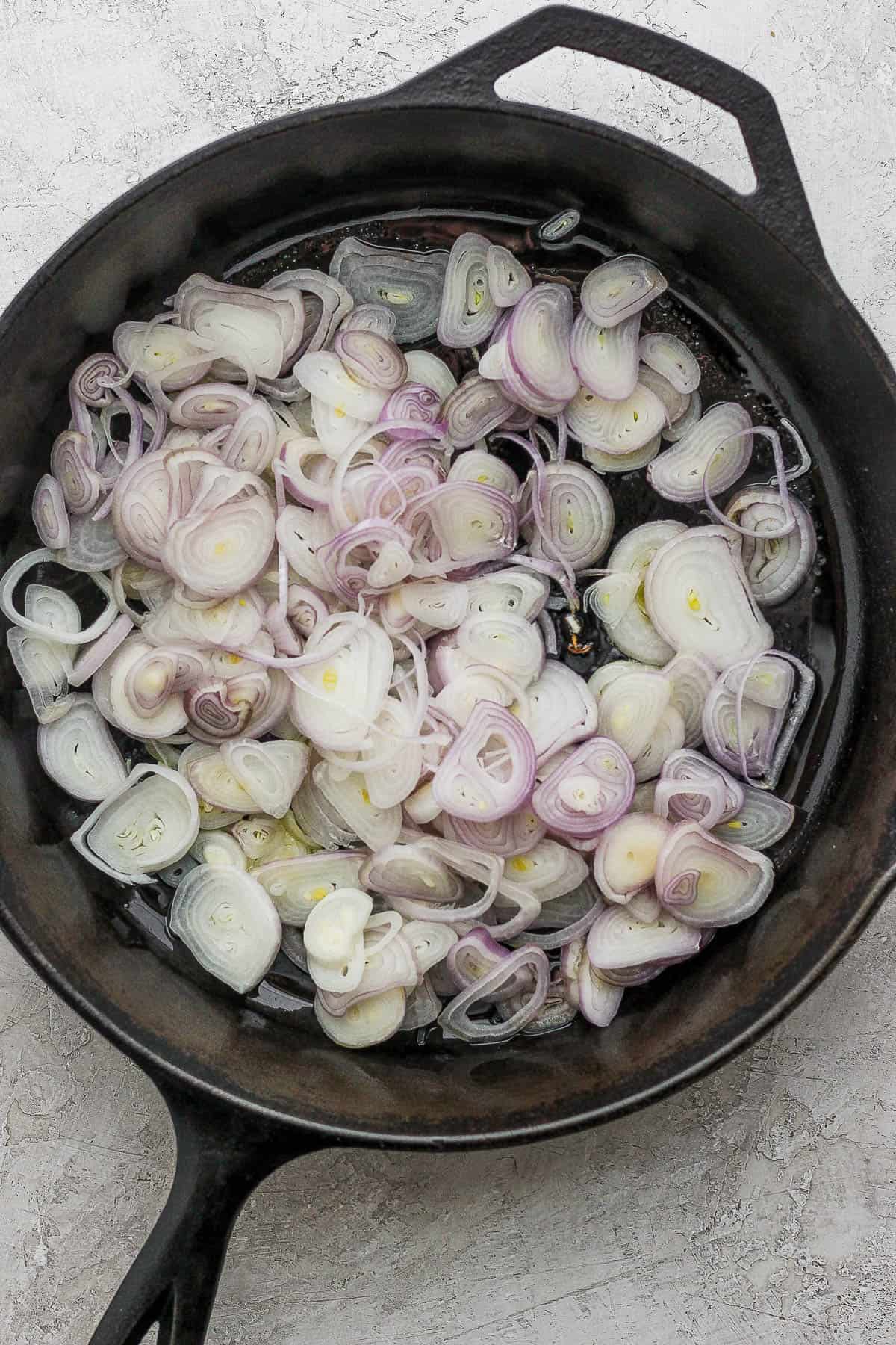 A large skillet with oil and sliced shallots.