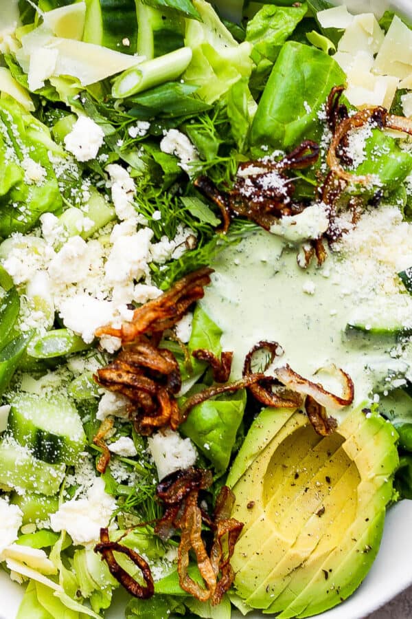 Top down shot of a bowl of green goddess salad with crispy shallots, avocado and green goddess dressing.
