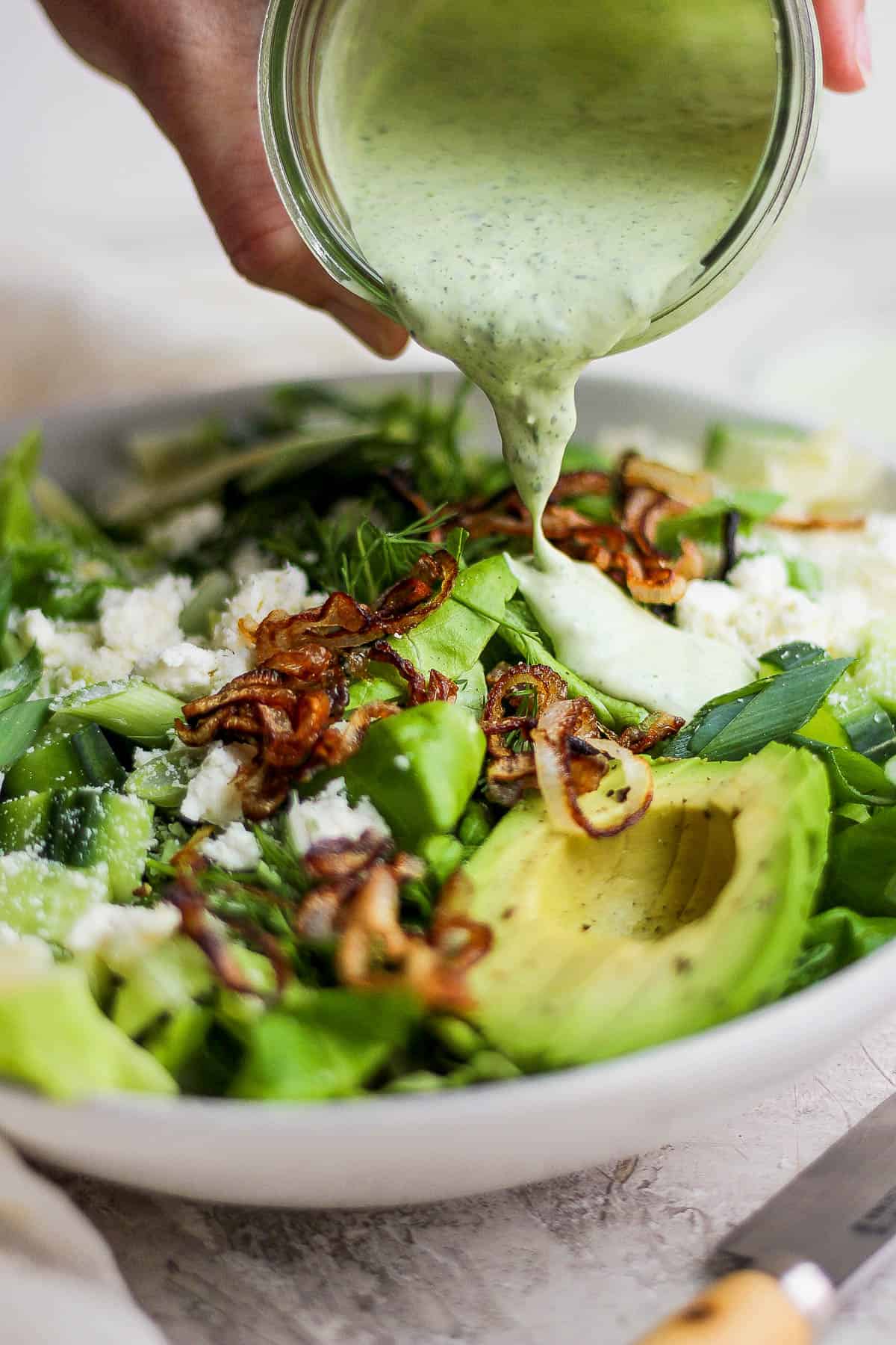Green goddess dressing being pour on to a fully topped green goddess salad.