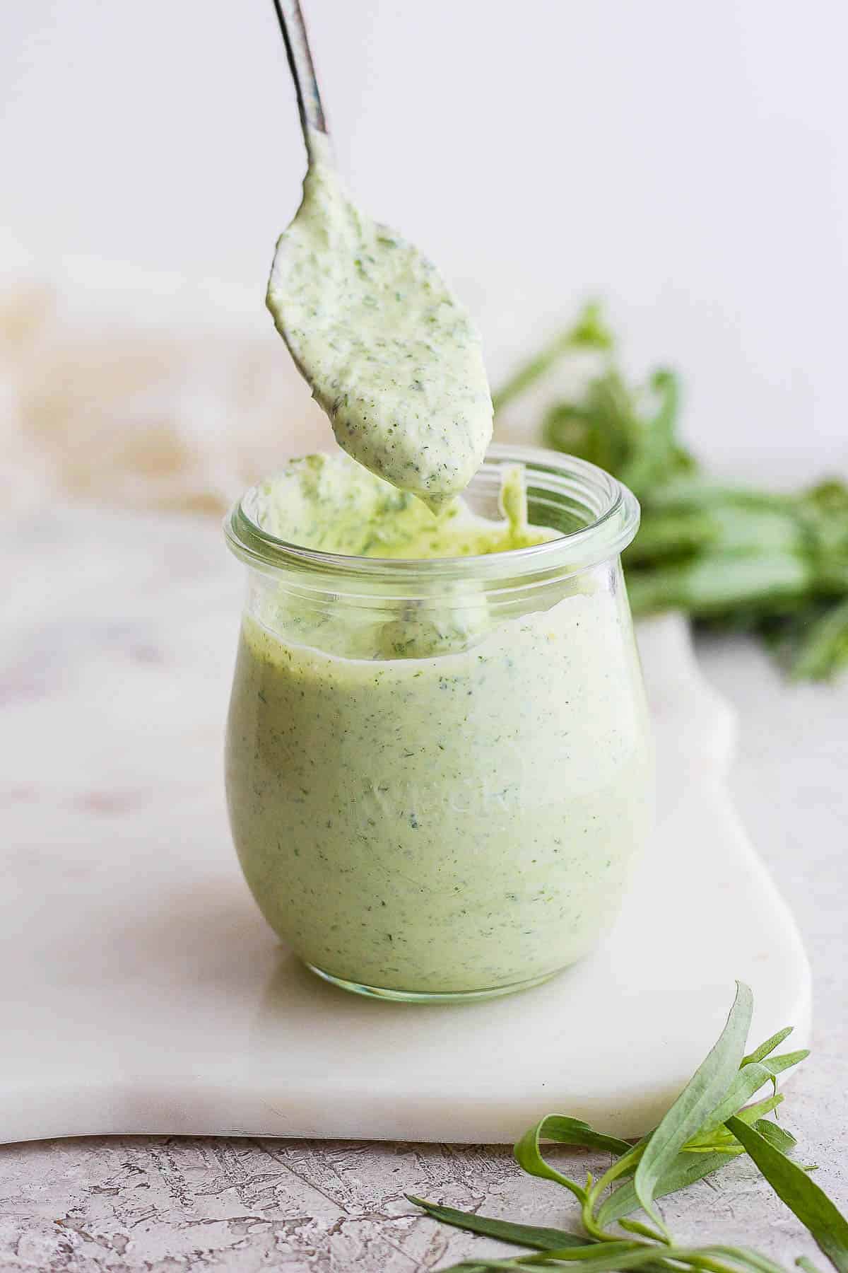 Green goddess salad dressing in a small jar and a spoon scooping some out.
