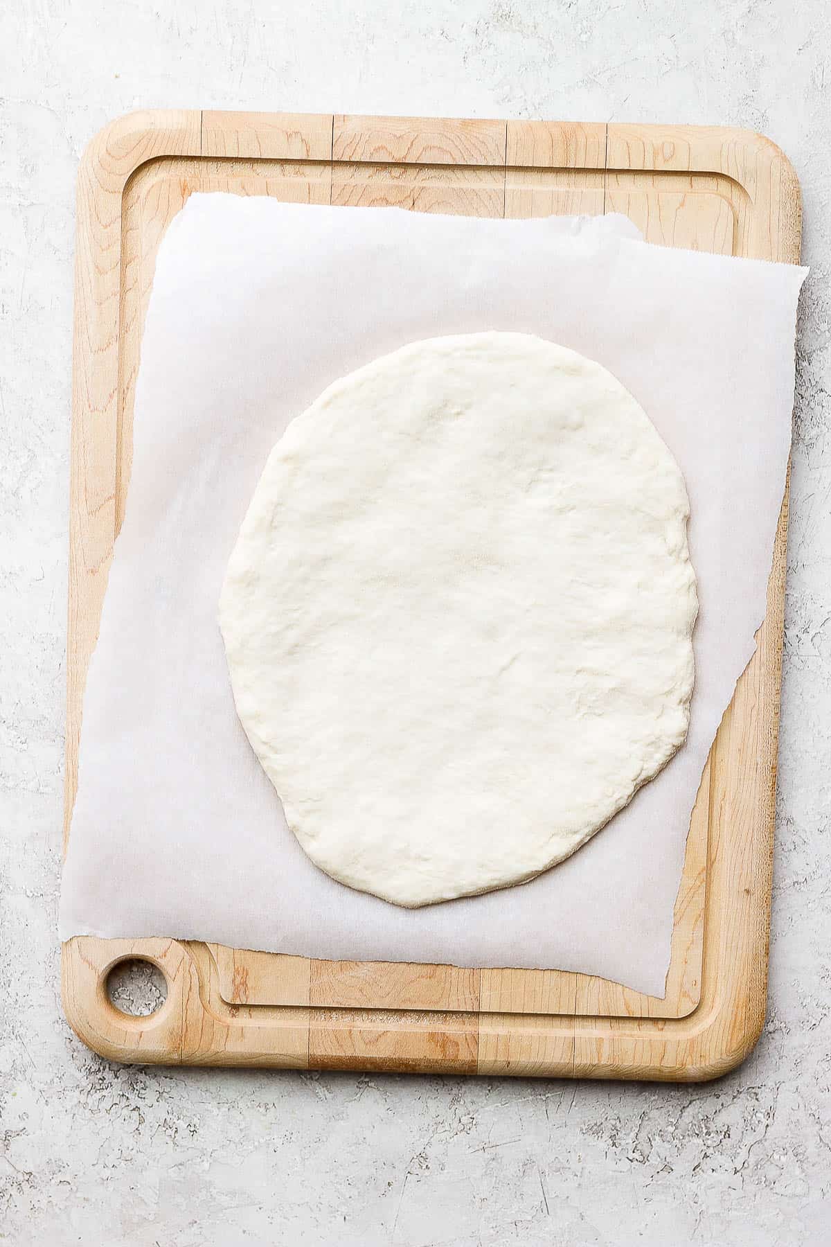 A portion of pizza dough spread out on top of parchment paper.