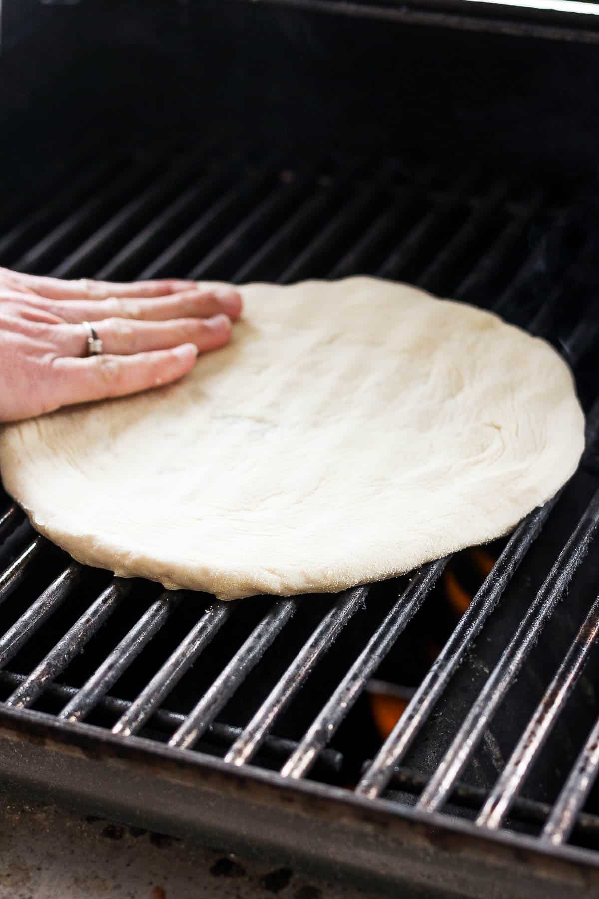 A portion of pizza dough on the grill grates.