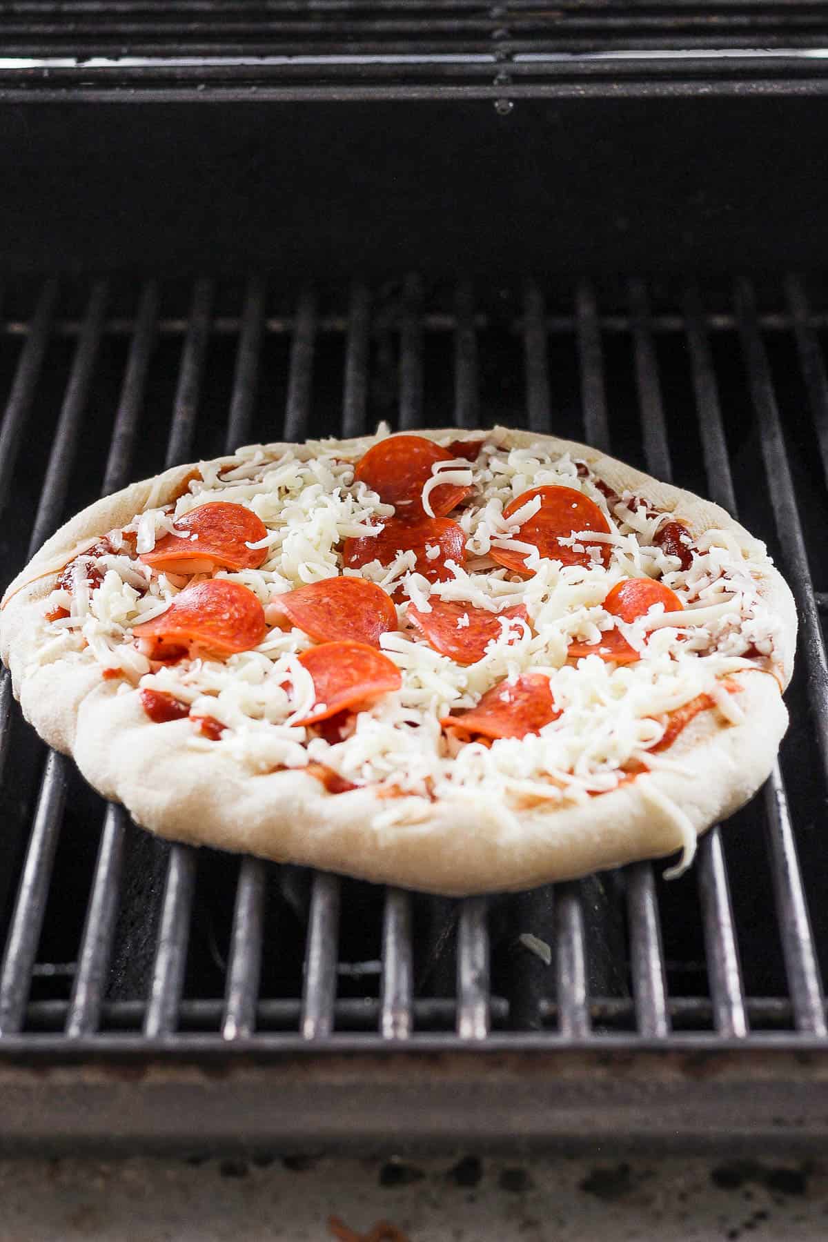 A fully topped pizza placed back on the grill.