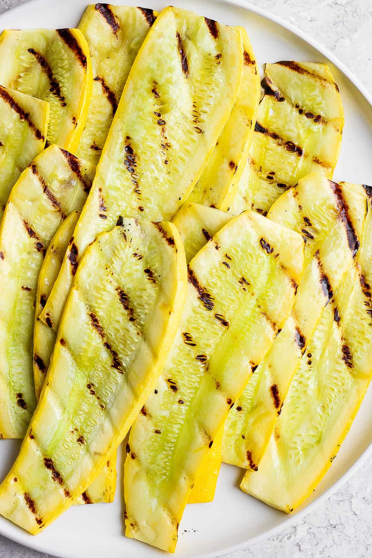 Perfectly grilled yellow squash on a white plate.