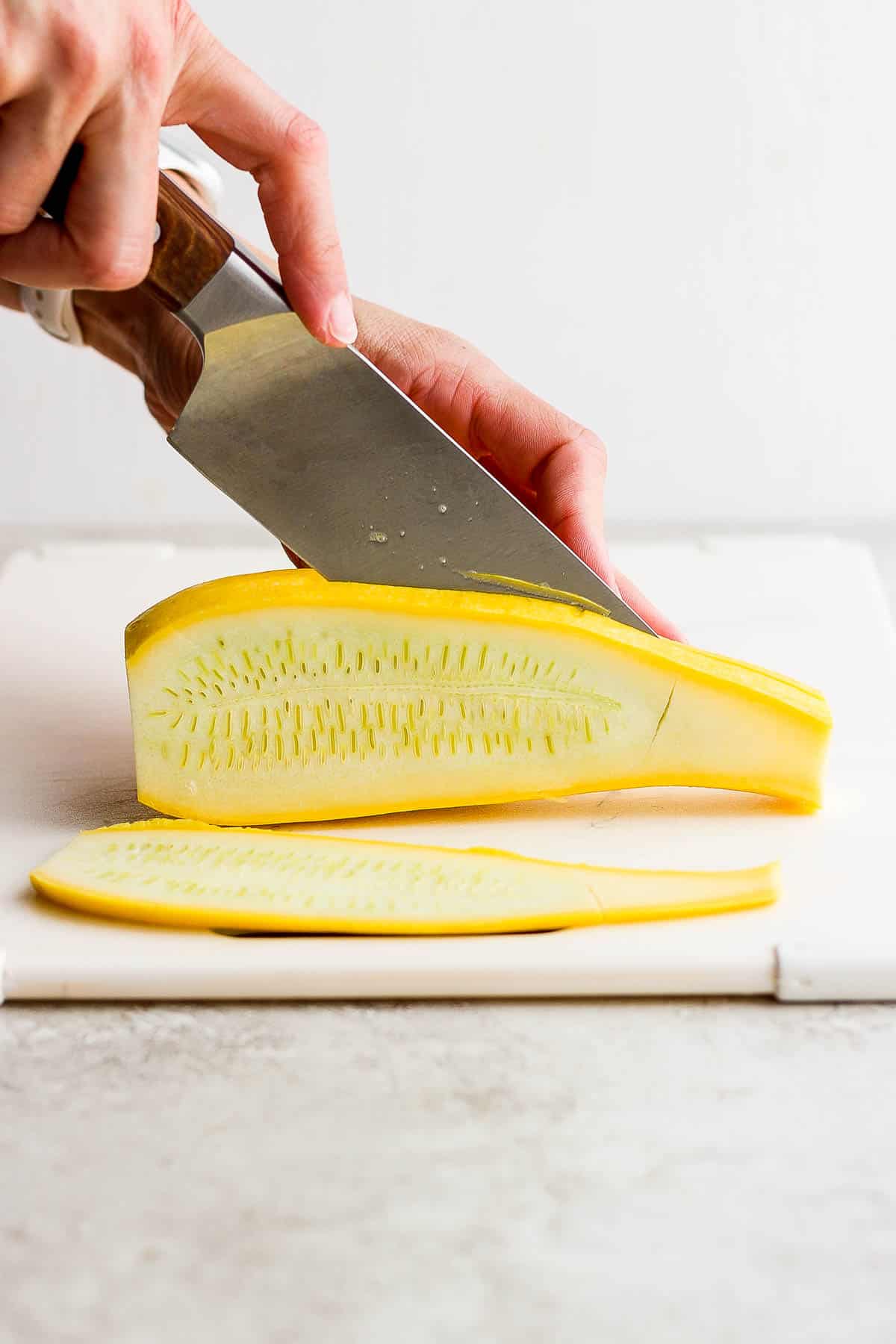 A large knife cutting a yellow squash into 1/2 inch planks.