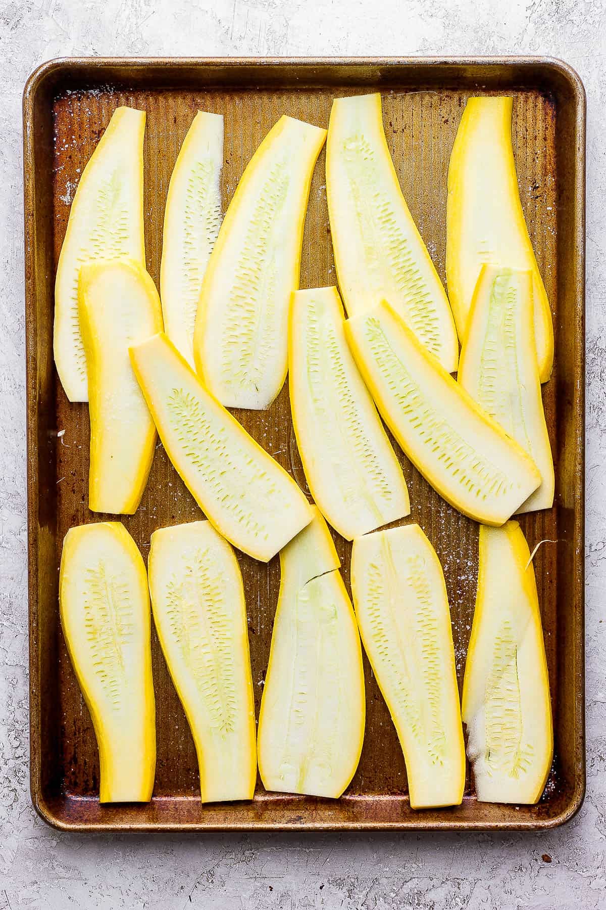 Seasoned yellow squash slabs on a large baking sheet.