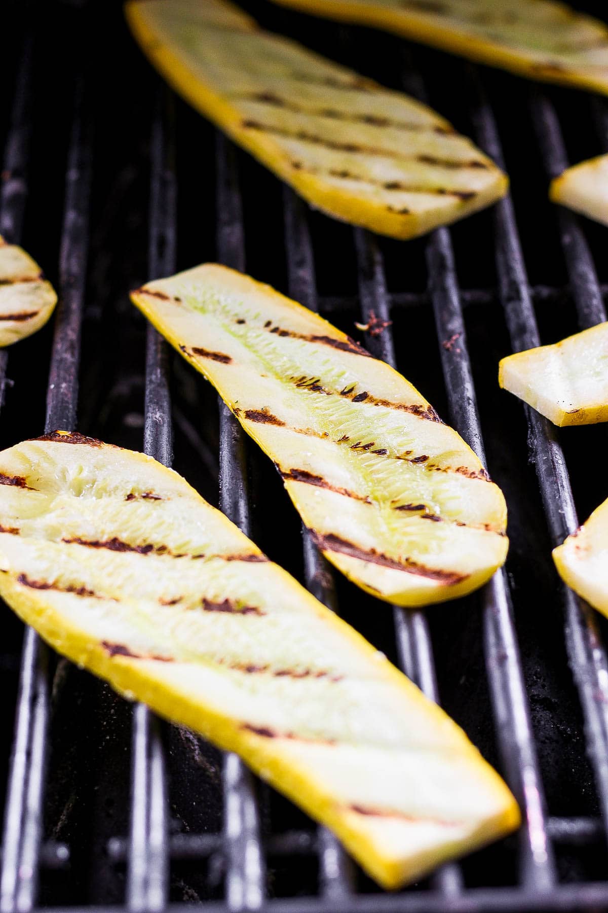 Slabs of yellow squash on the grill after being flipped.