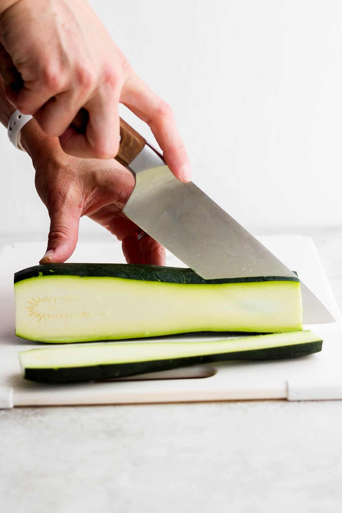 A zucchini being cut, lengthwise, into 1/2 inch slabs.