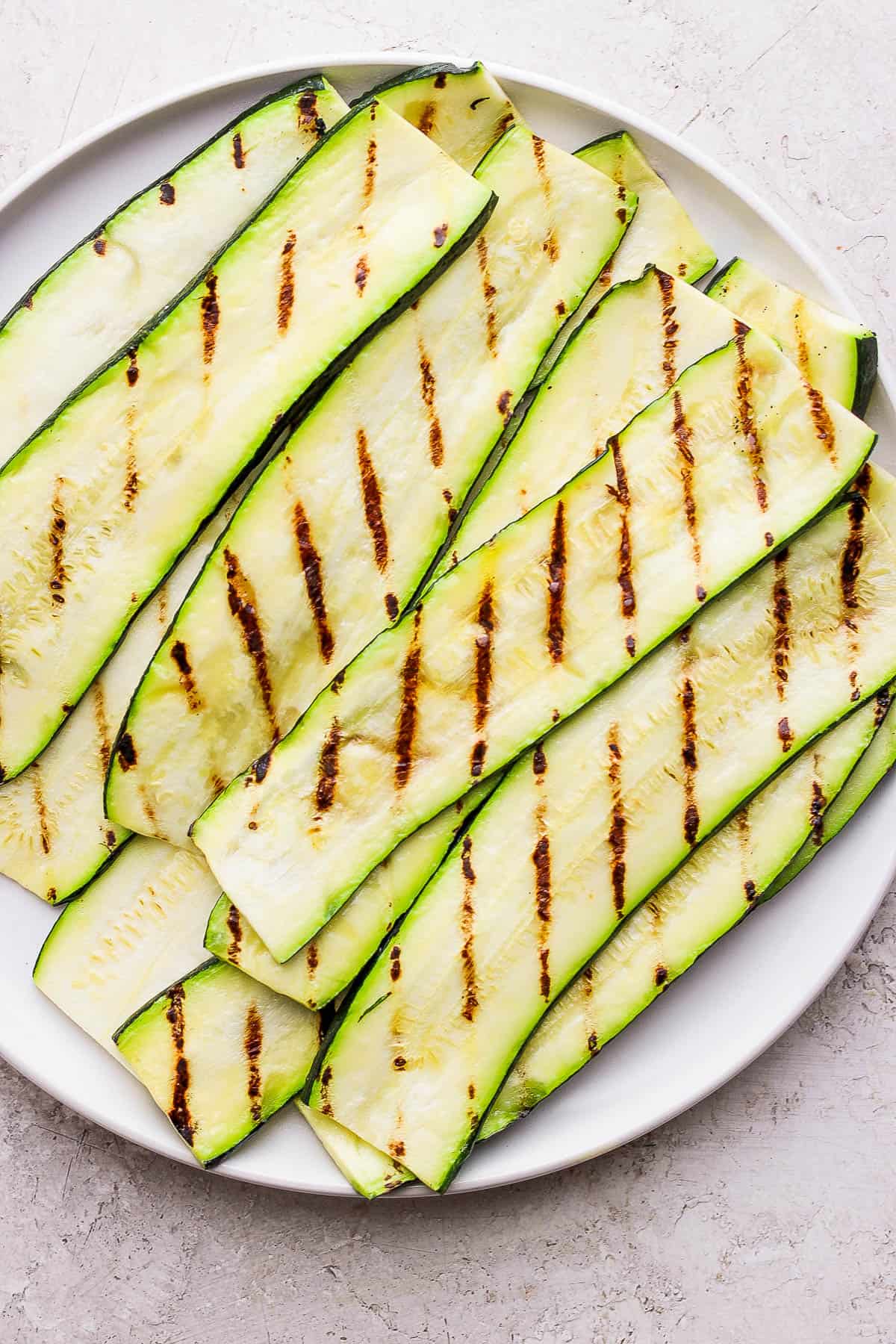 Perfectly grilled slabs of zucchini on a white plate.