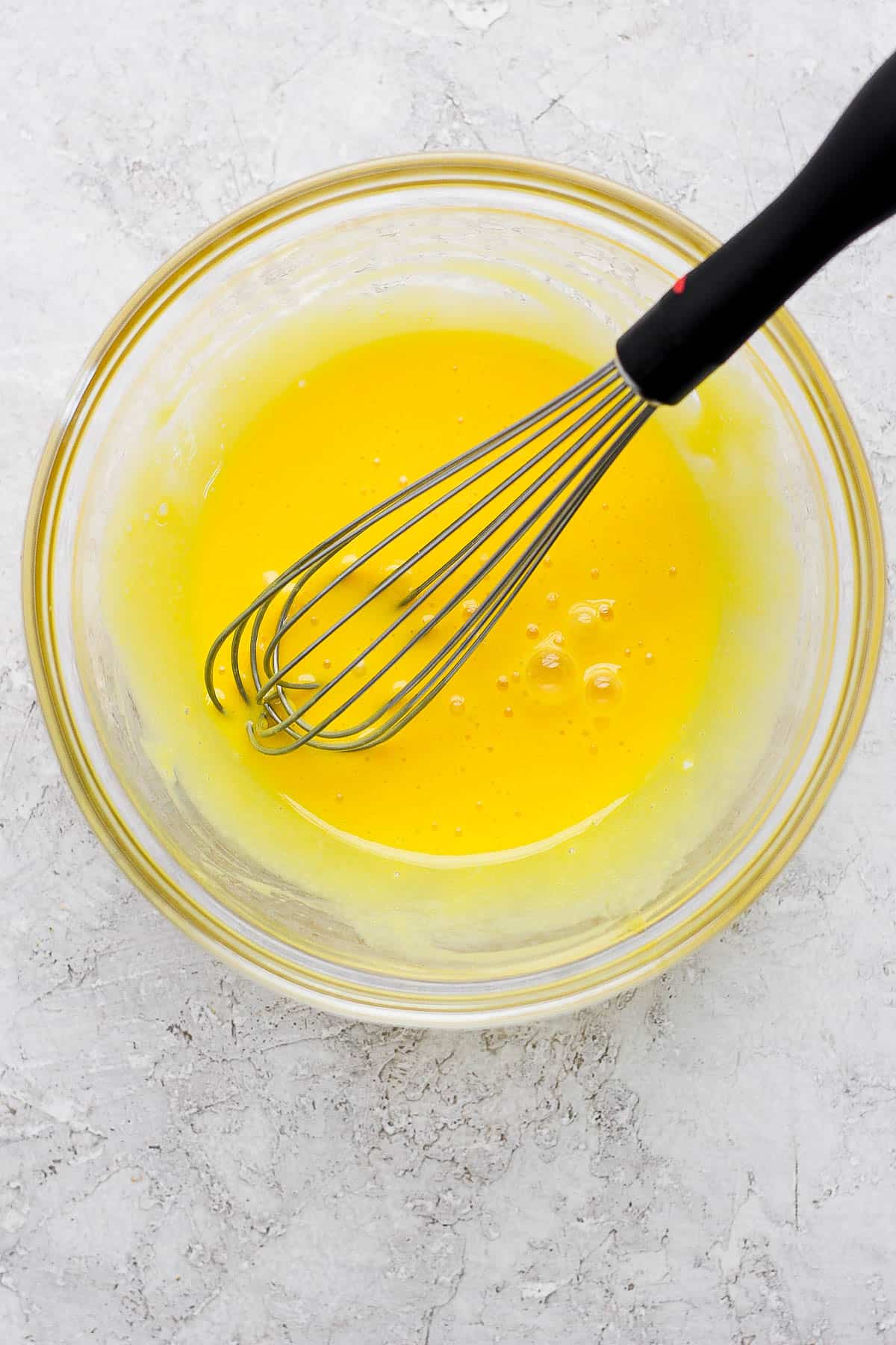 Egg yolks and lemon juice in a glass bowl with a whisk.