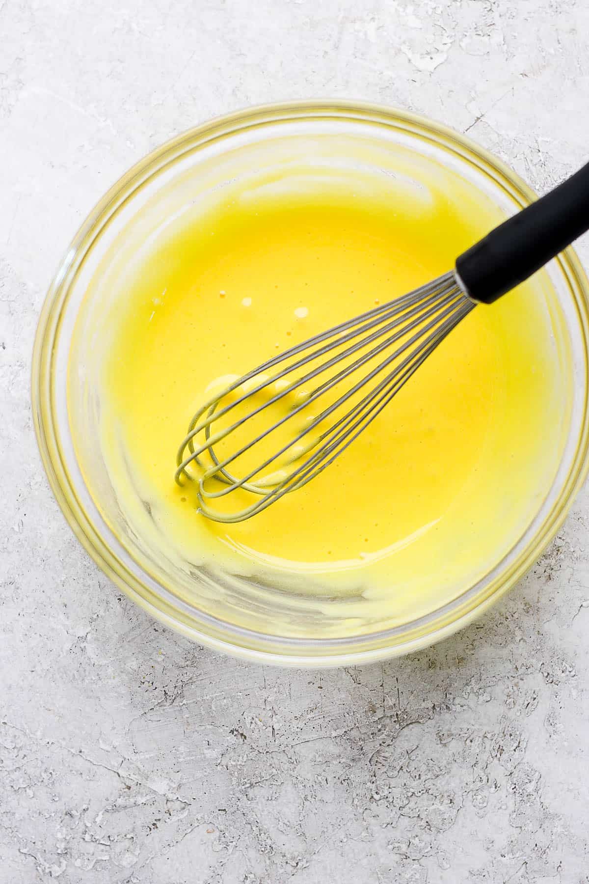 A glass bowl with egg yolks and lemon juice fully whisked together.