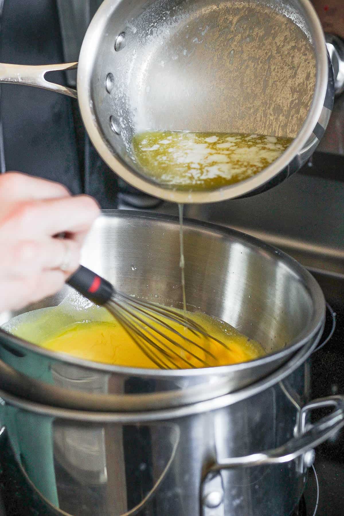 Hot melted butter being whisked into the egg yolk mixture.