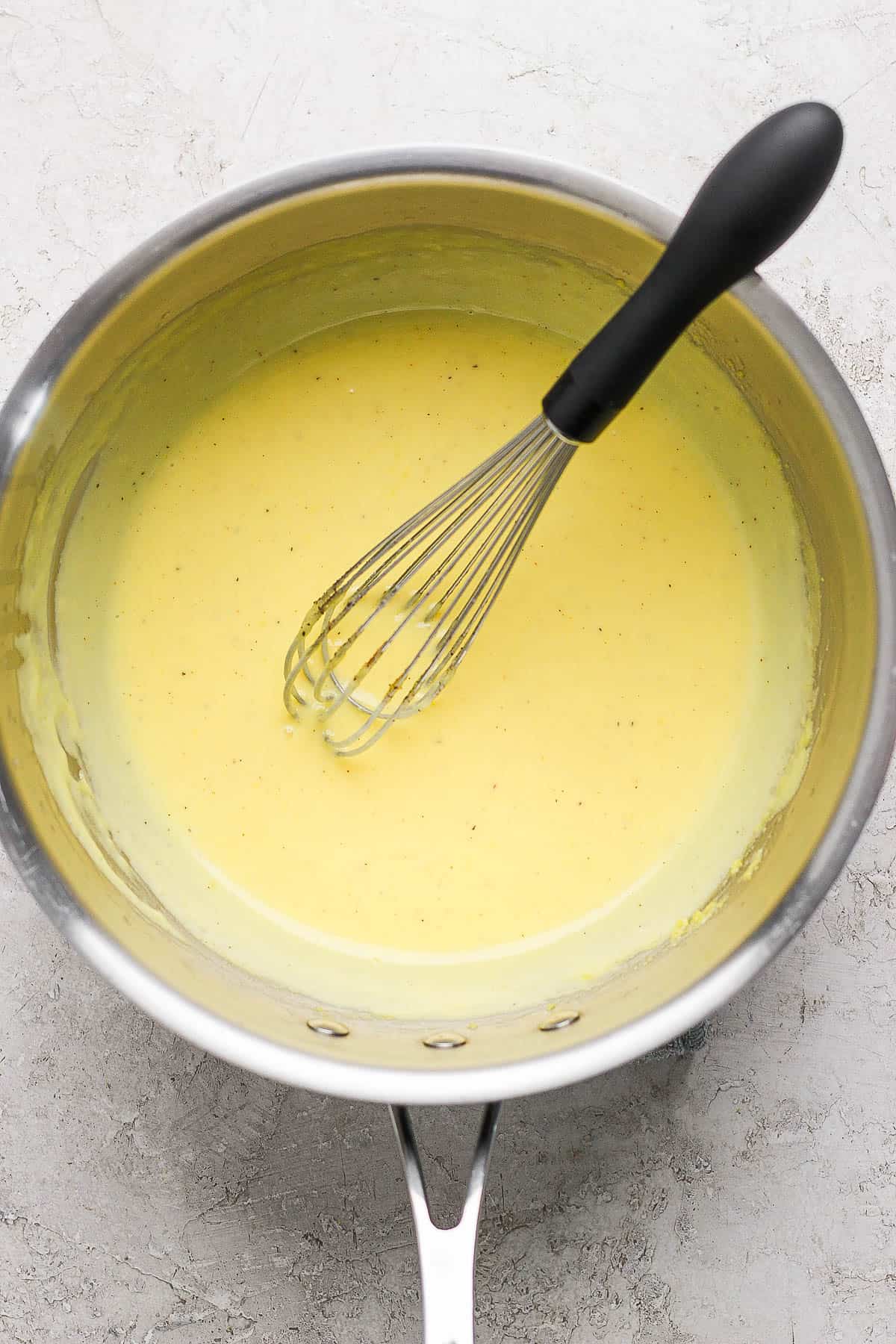 The hollandaise sauce in a saucepan with a whisk.