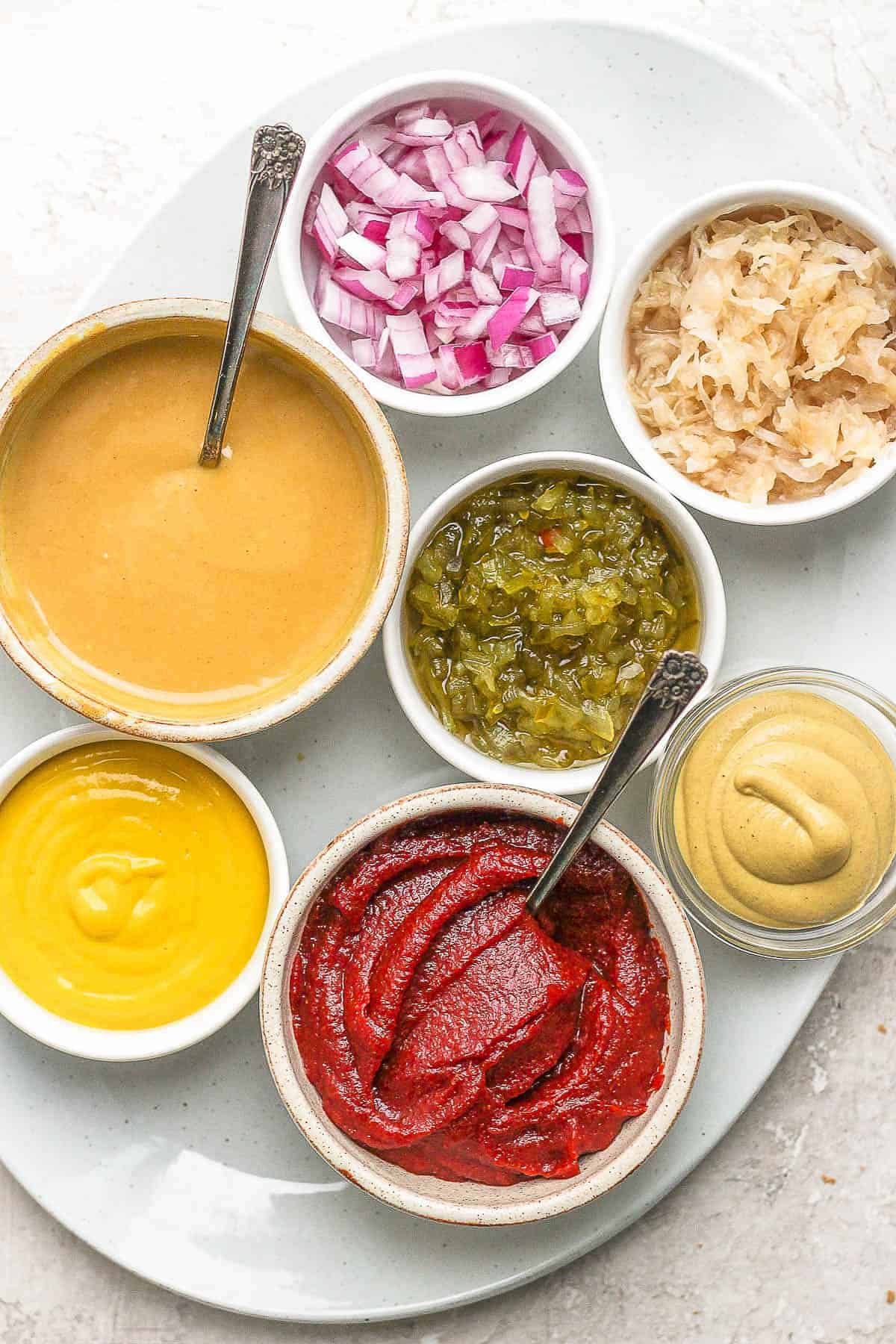 Brat toppings in small bowls on a large white plate.