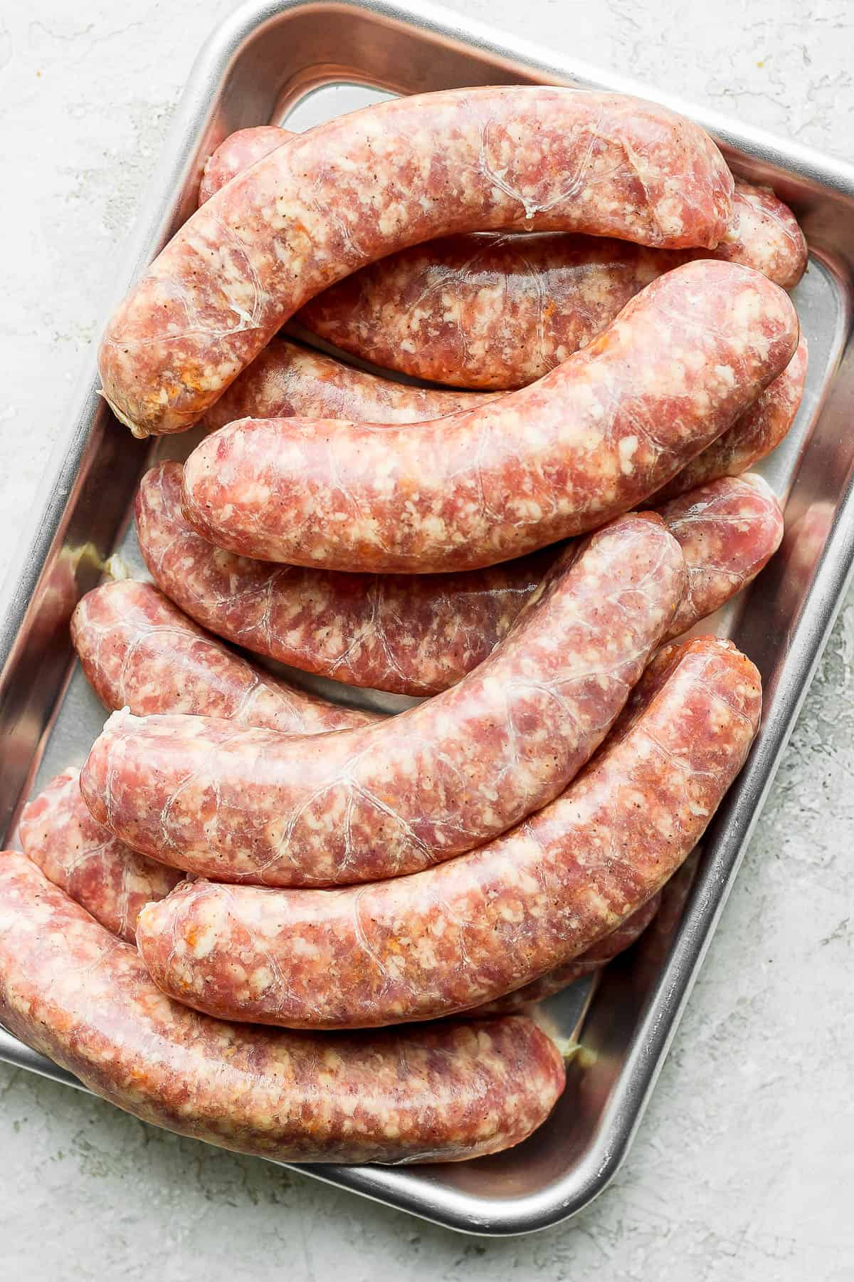 Uncooked brats on a metal tray.