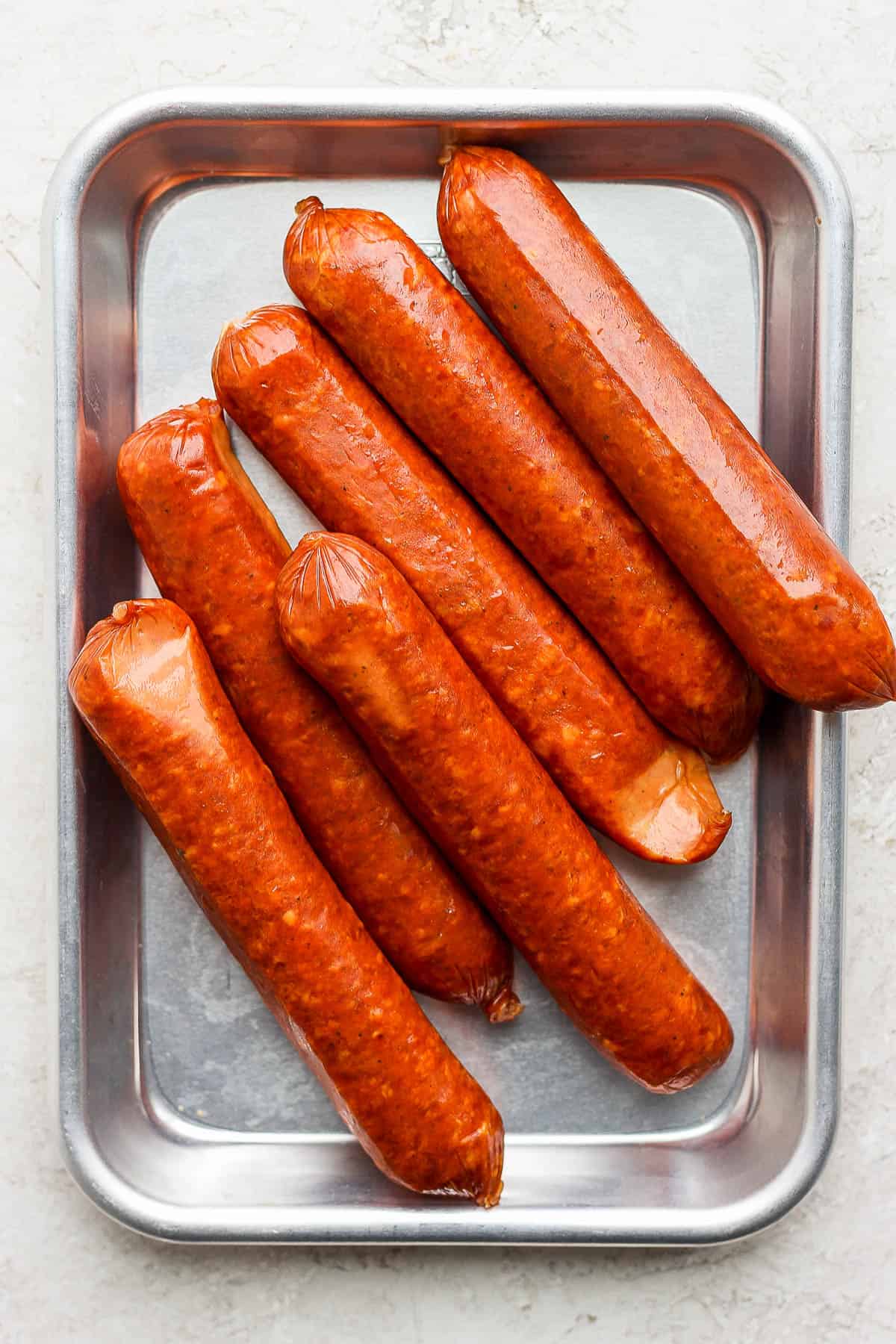 Precooked brats on a metal tray before grilling.