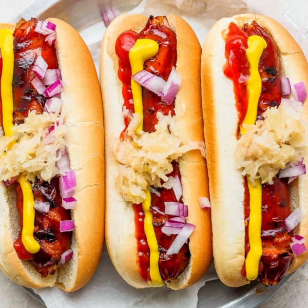 Top down shot of three grilled hot dogs in buns with ketchup, mustard, onion and saurkraut.