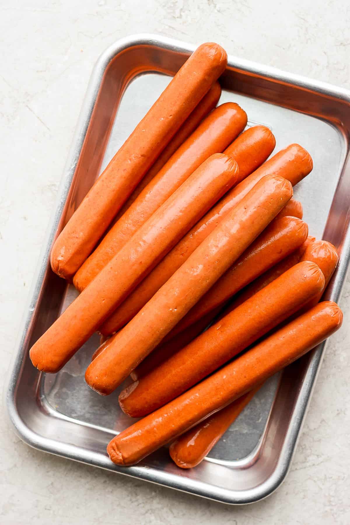Uncooked hot dogs in a small metal tray.