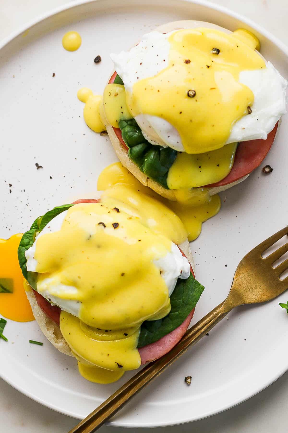 A top shot of eggs benedict on a white plate with a fork.