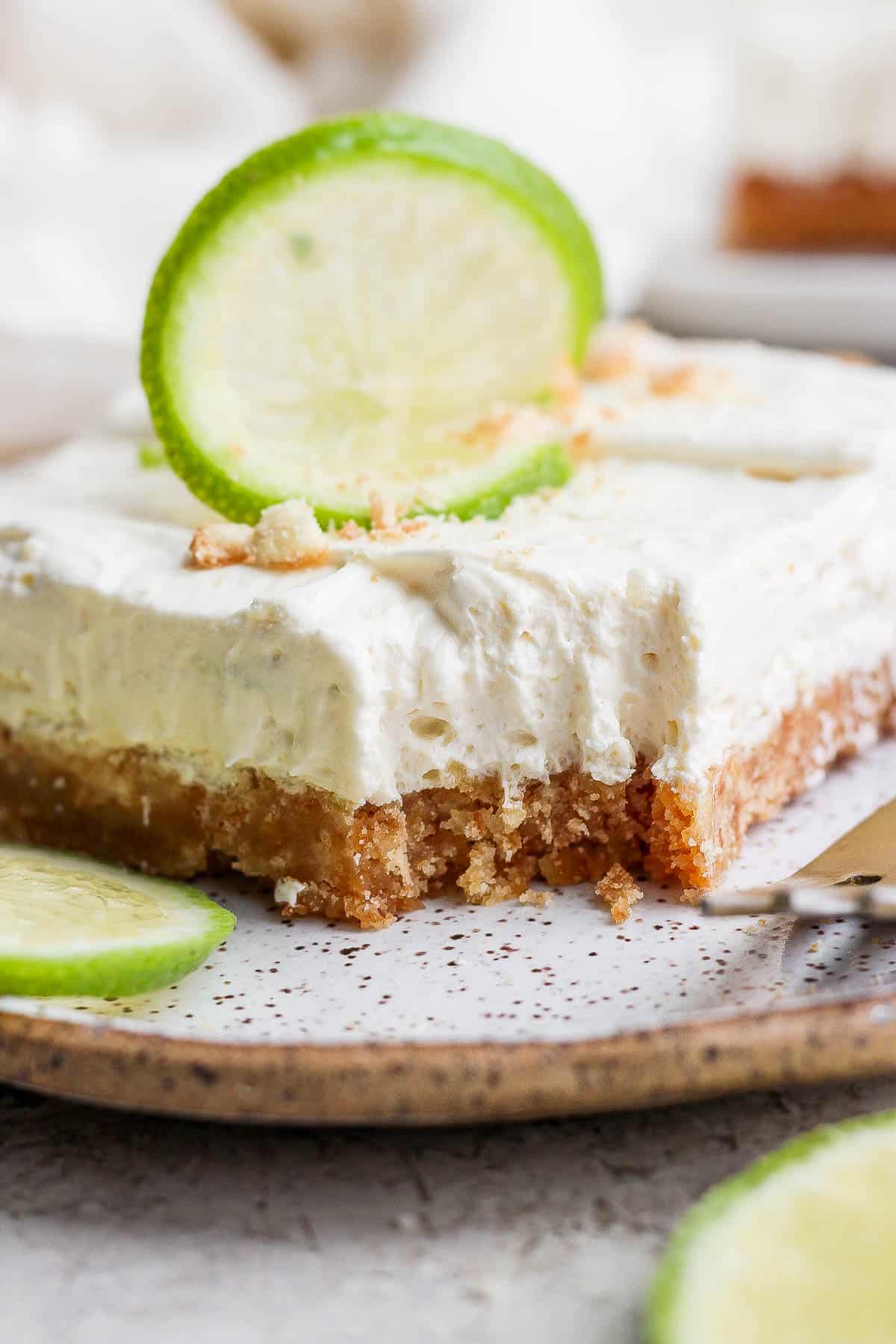 A square of the key lime cheese cake topped with a slice of lime on a plate.