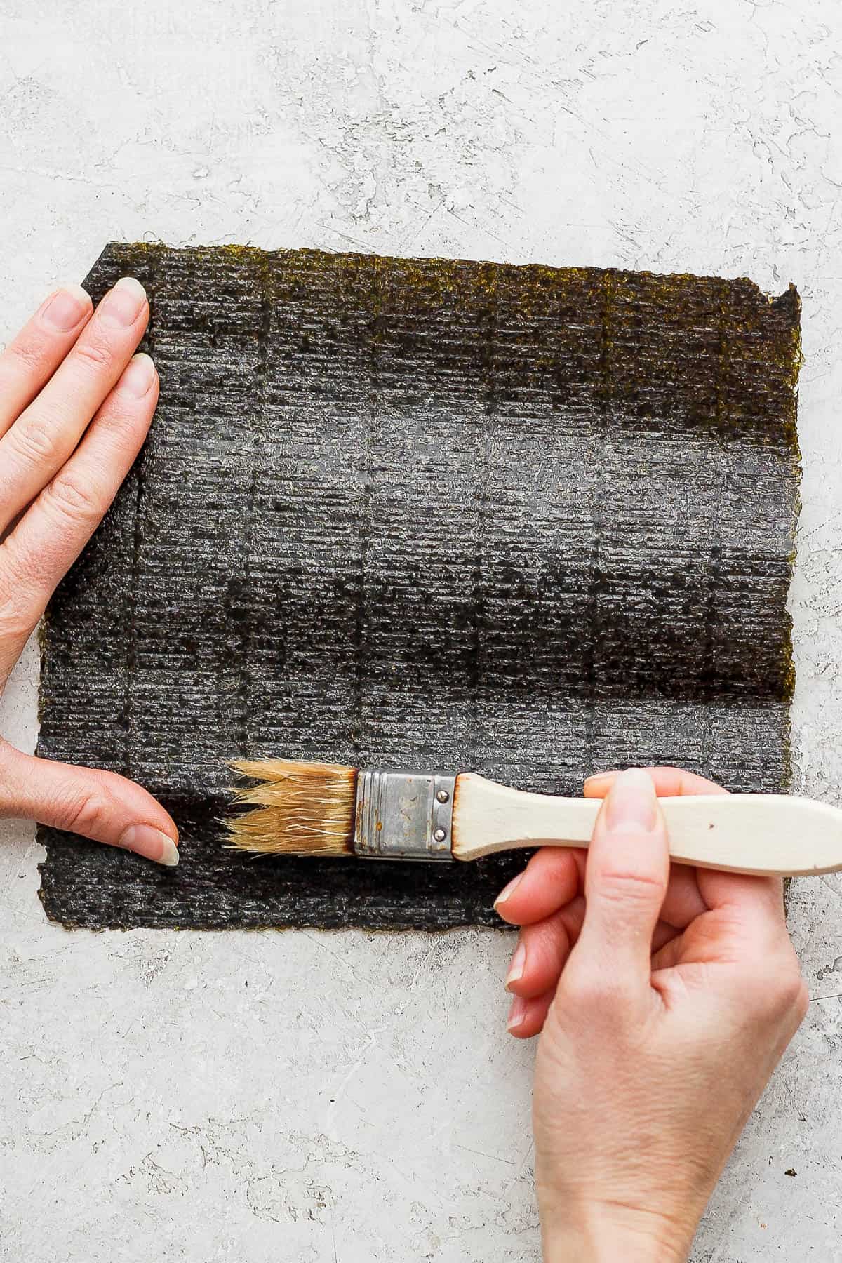 Water being brushed on the bottom inch of a nori sheet.