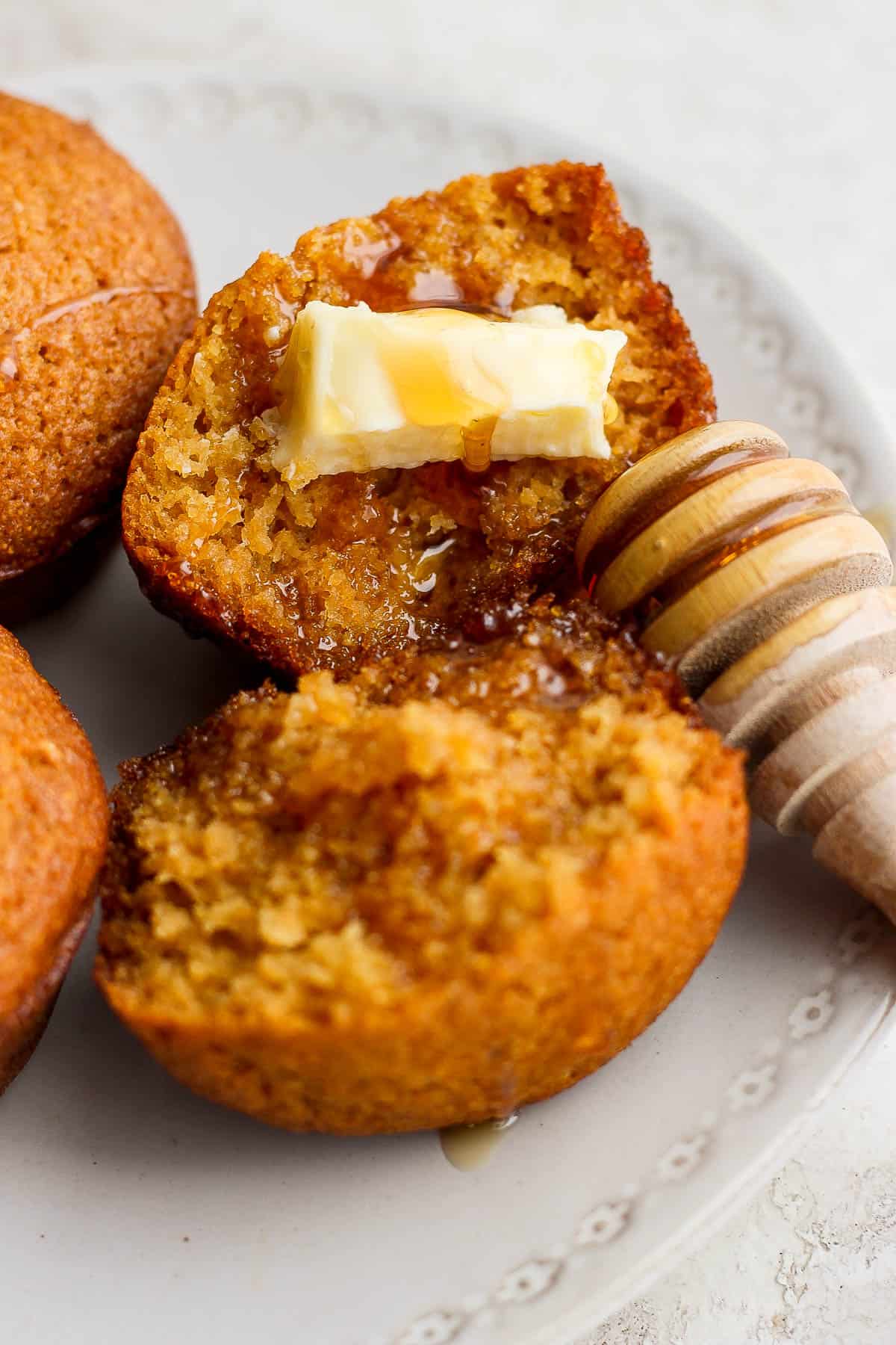 A cornbread muffin split in half with some butter and honey on top.