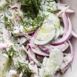 Close up shot of a creamy cucumber salad in a bowl with fresh dill on top.