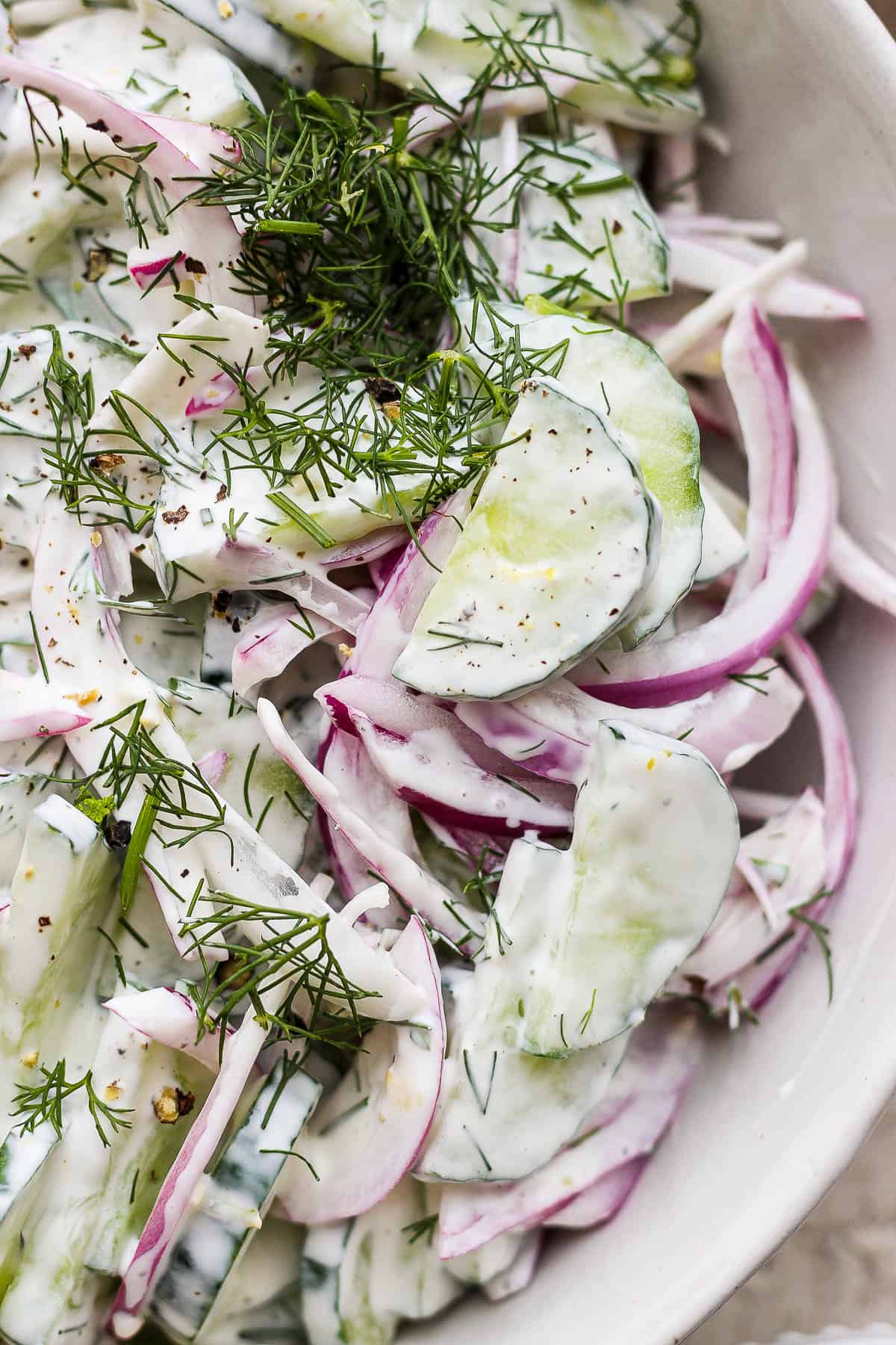 A close up of the creamy cucumber salad in the bowl topped with freshly chopped dill.