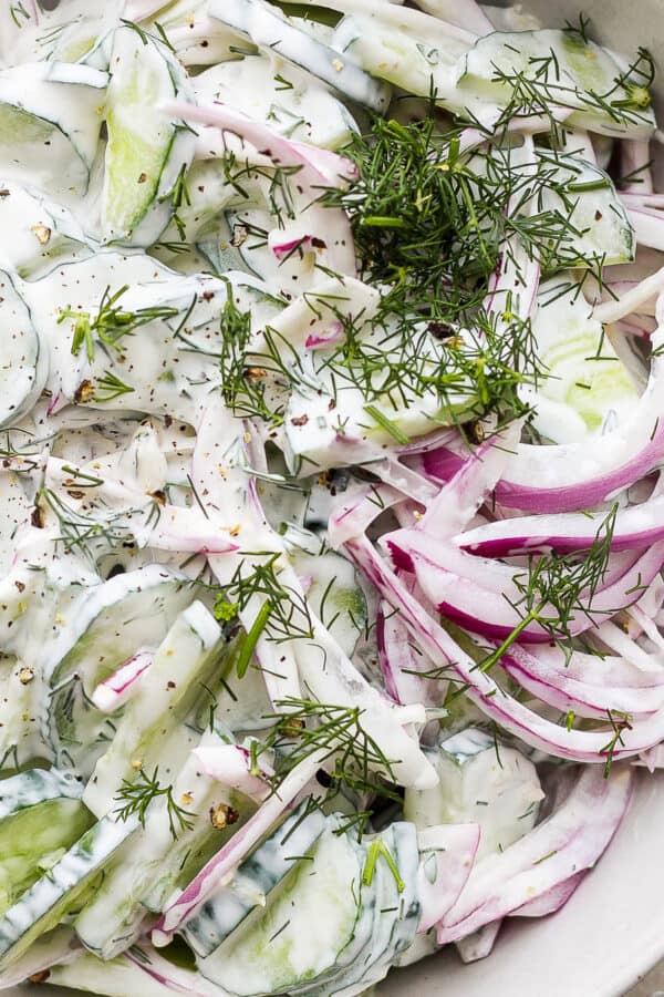 Close up shot of a creamy cucumber salad in a bowl with fresh dill on top.
