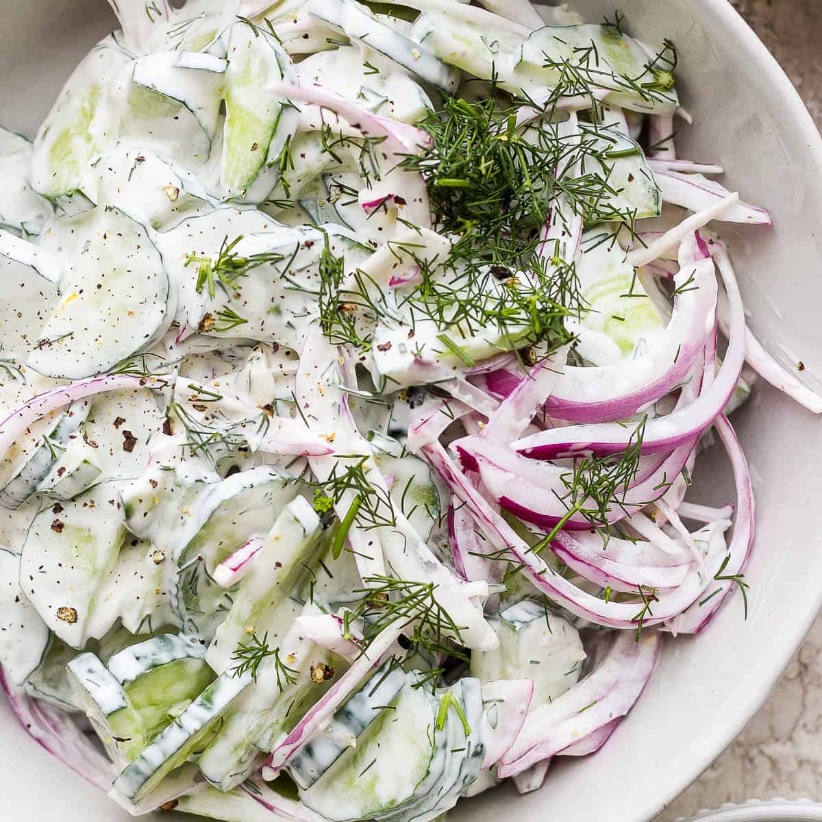 Close up shot of a creamy cucumber salad in a bowl with fresh dill on top.