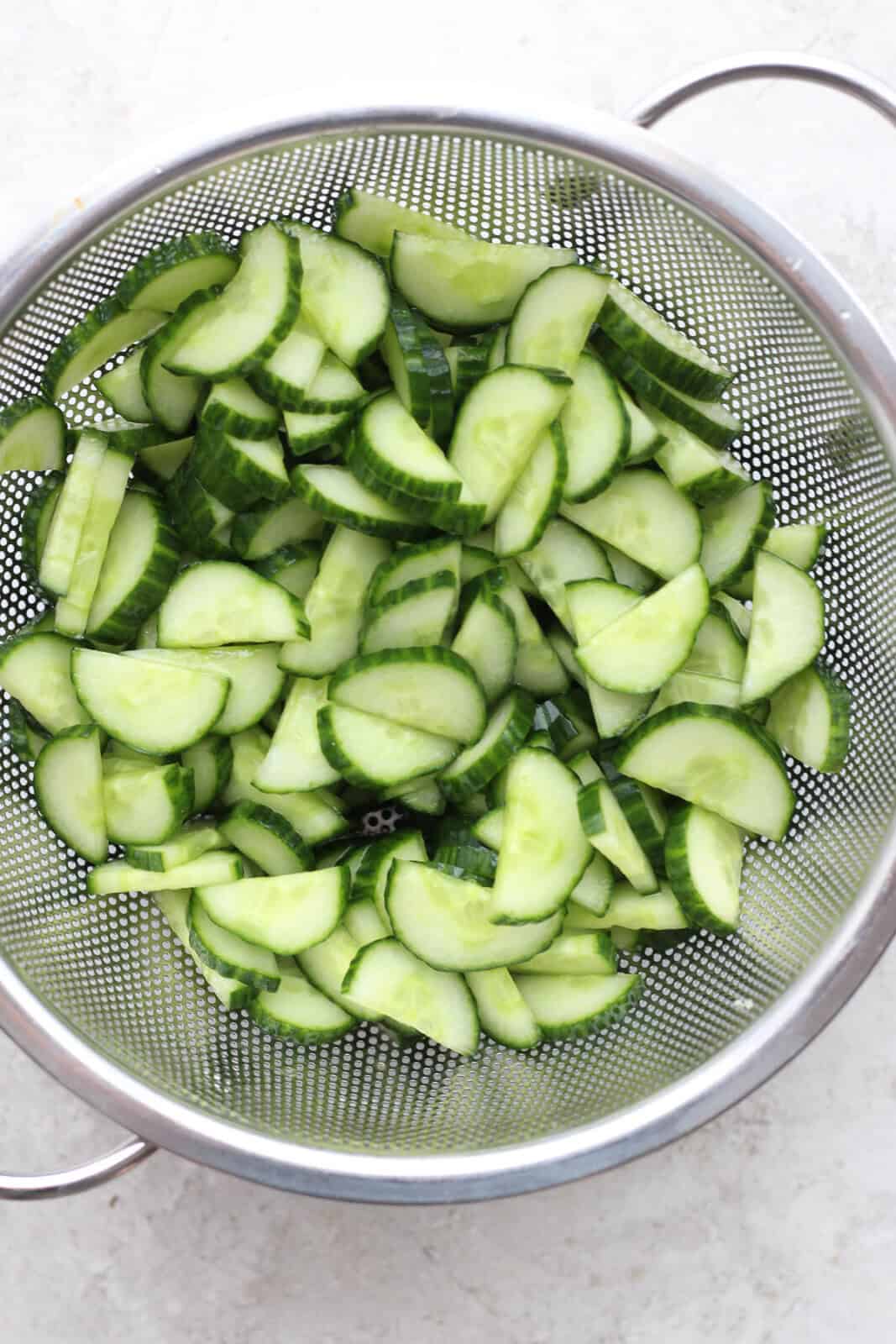 Sliced and halved cucumbers in a colander to make creamy cucumber salad with sour cream and mayo.