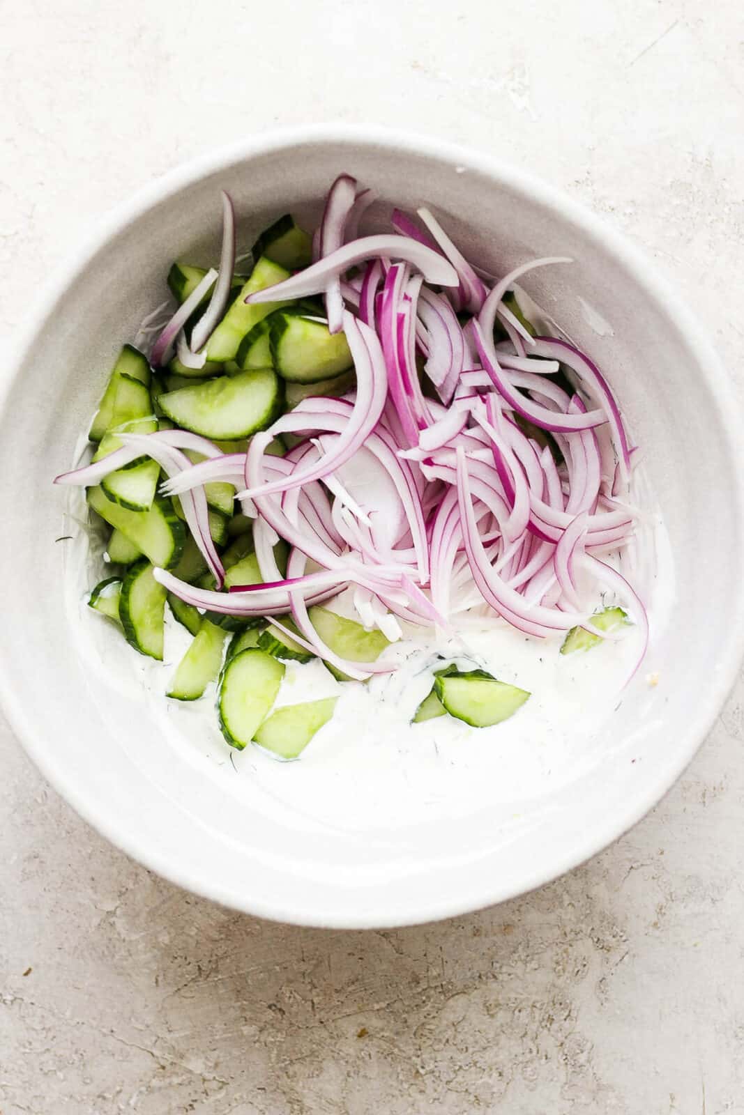 Prepped onions and cucumbers in cream mixture to make creamy cucumber salad with sour cream and mayo.