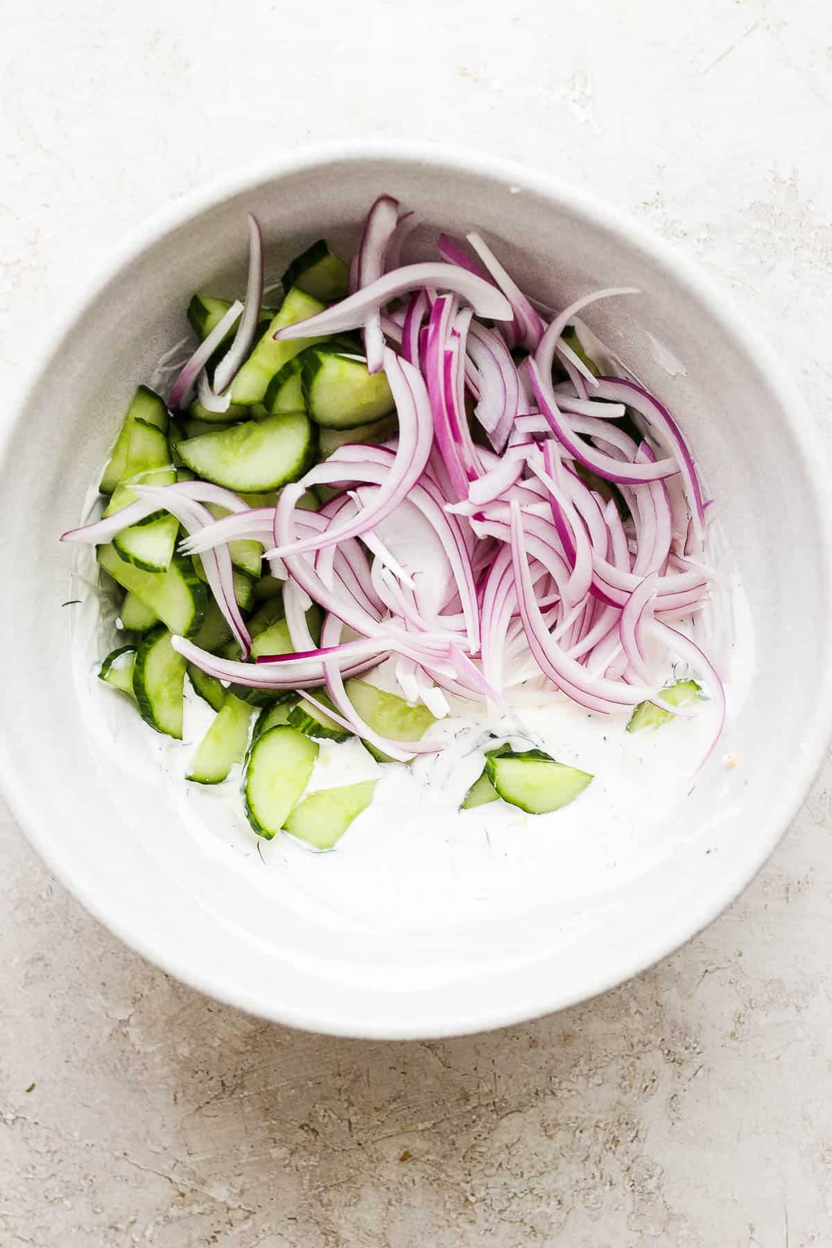 Cucumbers and red onion added to the sour cream mixture in the same large bowl.
