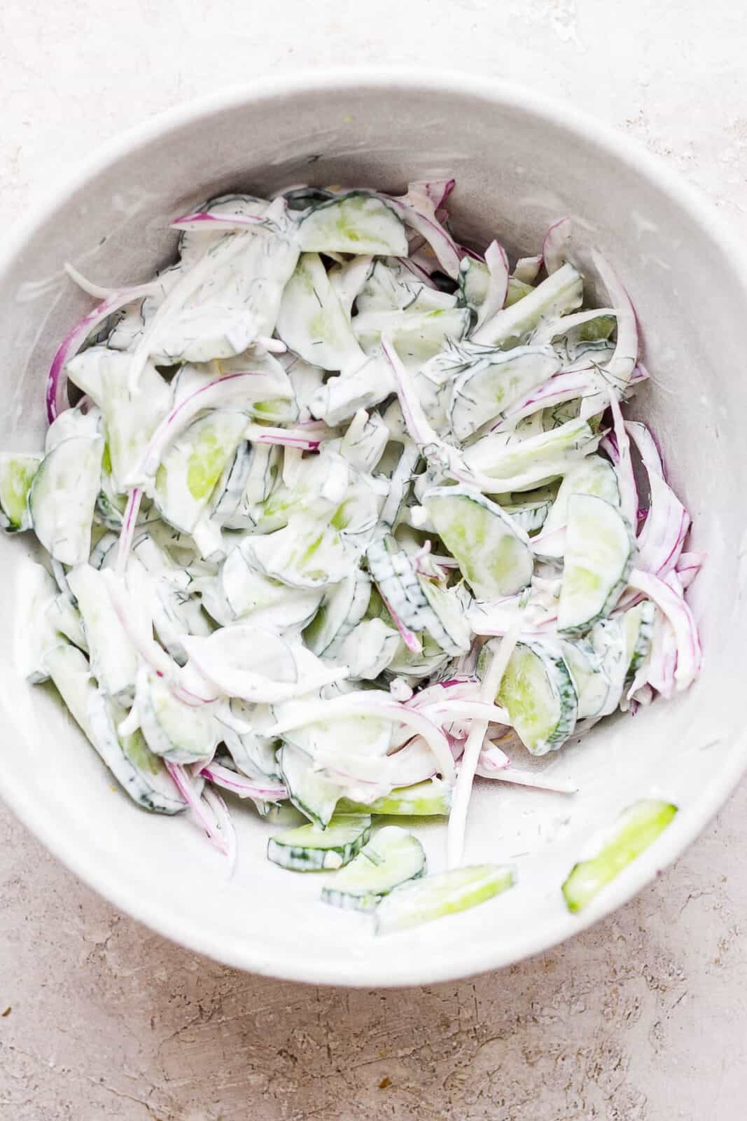 creamy cucumber salad with sour cream and mayo mixed together in a bowl.